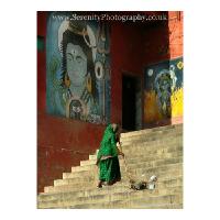 A woman sweeps the steps leading to the ghats along the Ganges, overlooked by paintings of Gods. Varanasi, India.