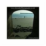 A man walks his dogs along Folkestone beach; framed by an arch. Kent, England.